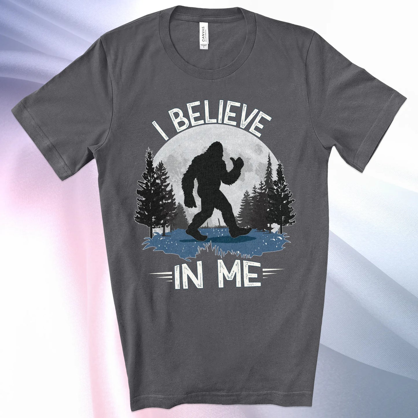 Asphalt colored Bigfoot Believes T-Shirt with Bigfoot's silhouette in a moonlit forest and I Believe at the top and In Me below