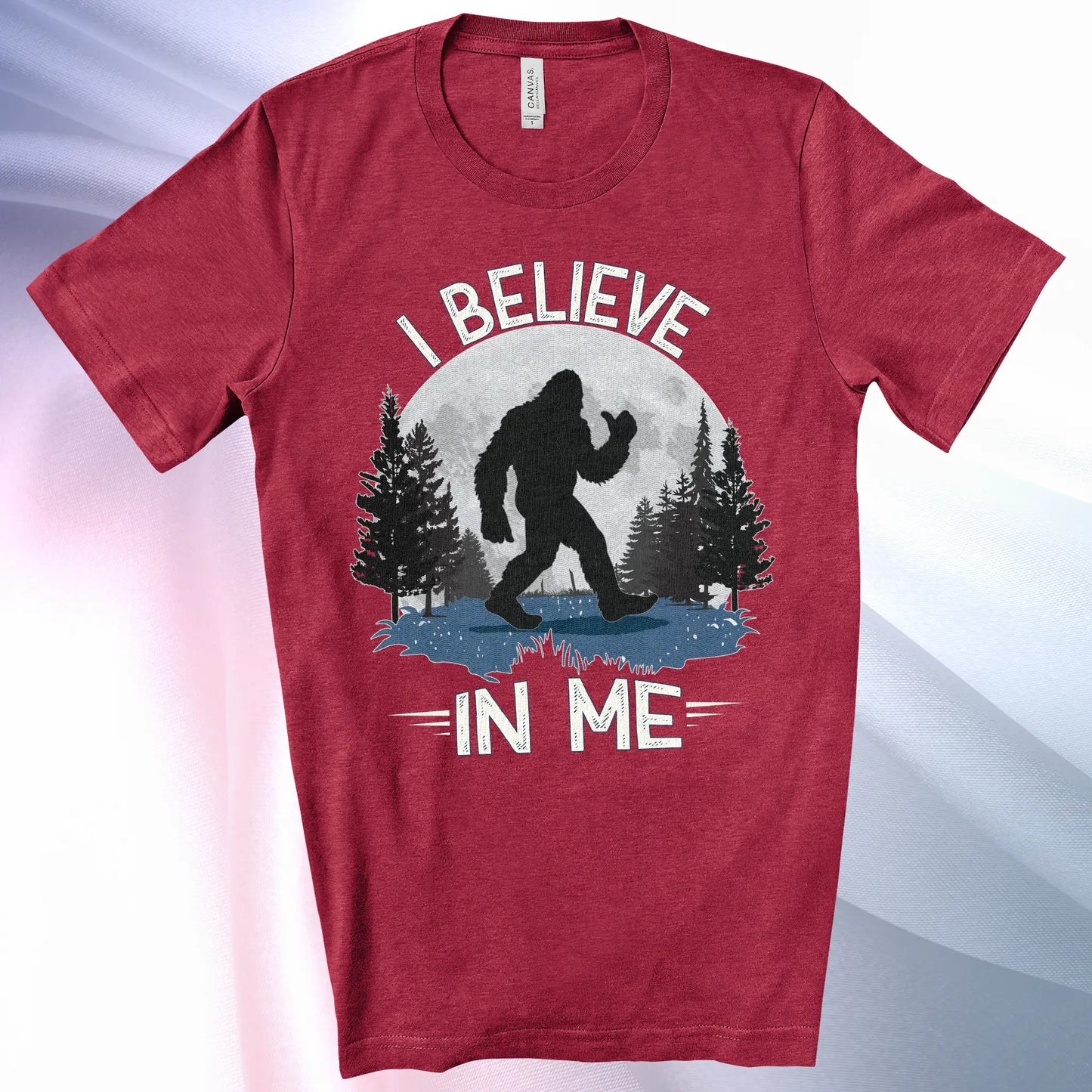 Heather Raspberry Bigfoot Believes T-Shirt with Bigfoot's silhouette in a moonlit forest and I Believe at the top and In Me below