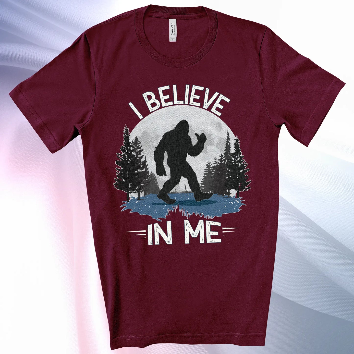 Maroon Bigfoot Believes T-Shirt with Bigfoot's silhouette in a moonlit forest and I Believe at the top and In Me below