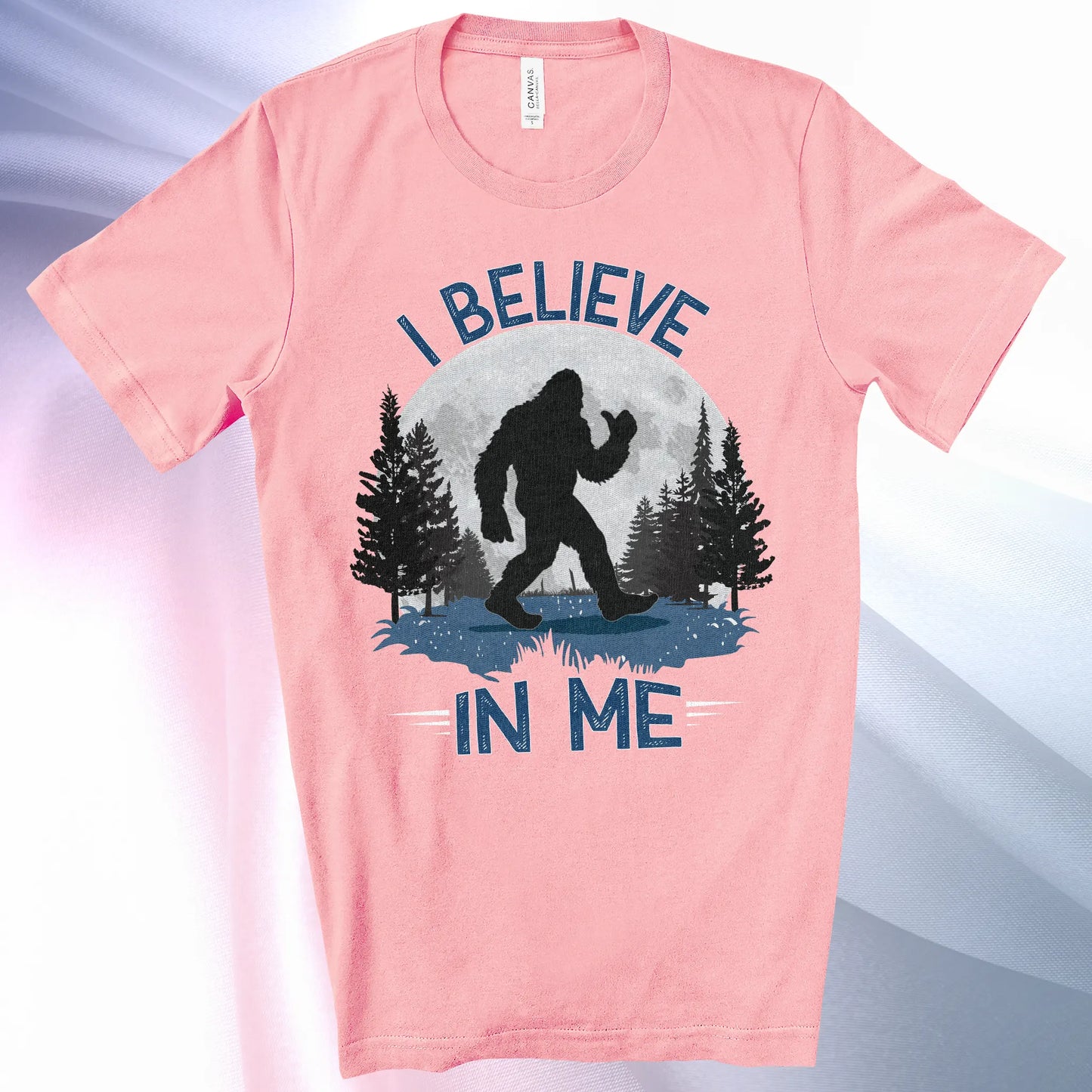 Pink colored Bigfoot Believes T-Shirt with Bigfoot's silhouette in a moonlit forest and I Believe at the top and In Me below