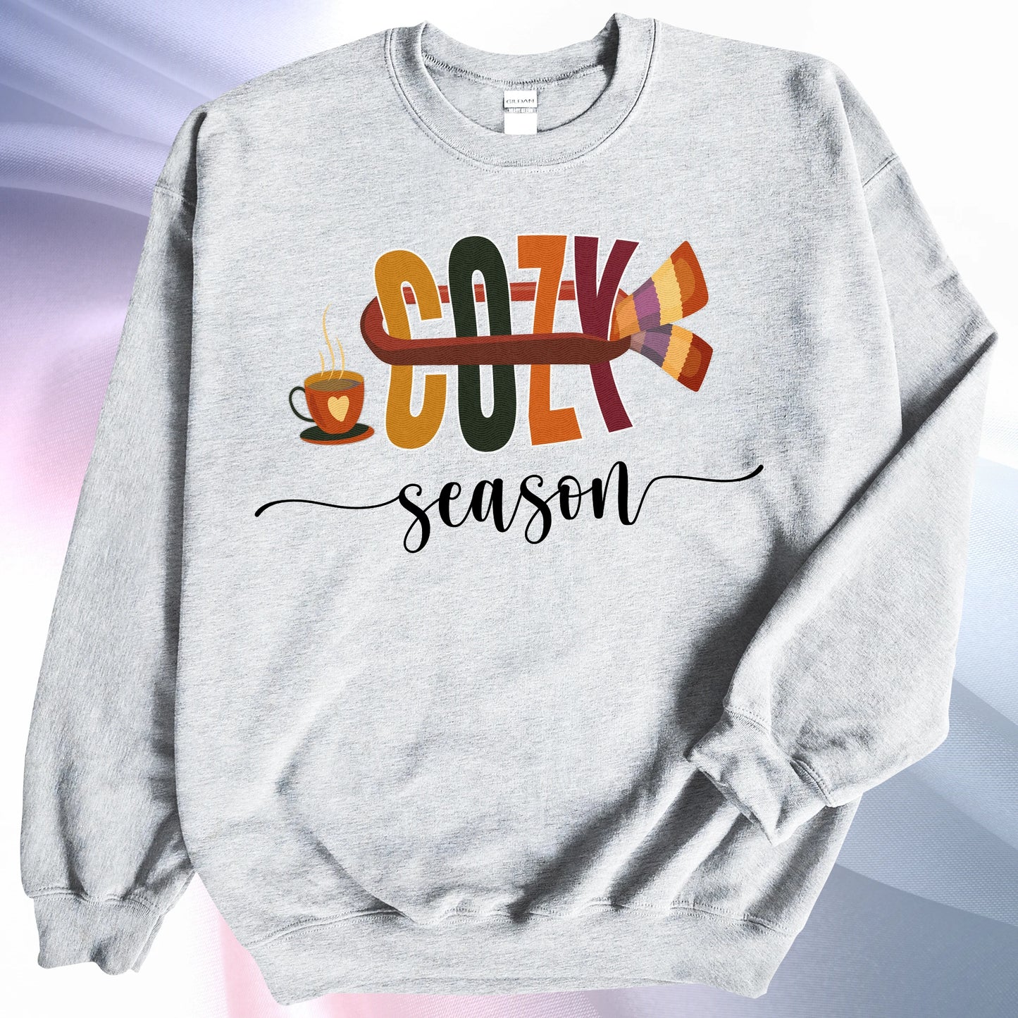 Ash colored Cozy Season sweatshirt, on colorful gradient silk background. Left sleeve is folded over the garment at the elbow