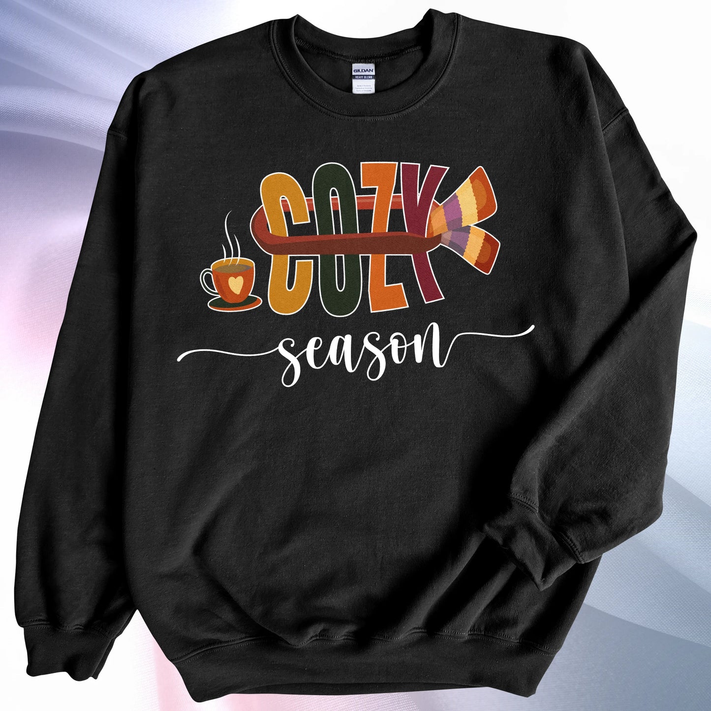 Black Cozy Season sweatshirt, placed on colorful gradient silk background. Left sleeve folded over the garment at the elbow