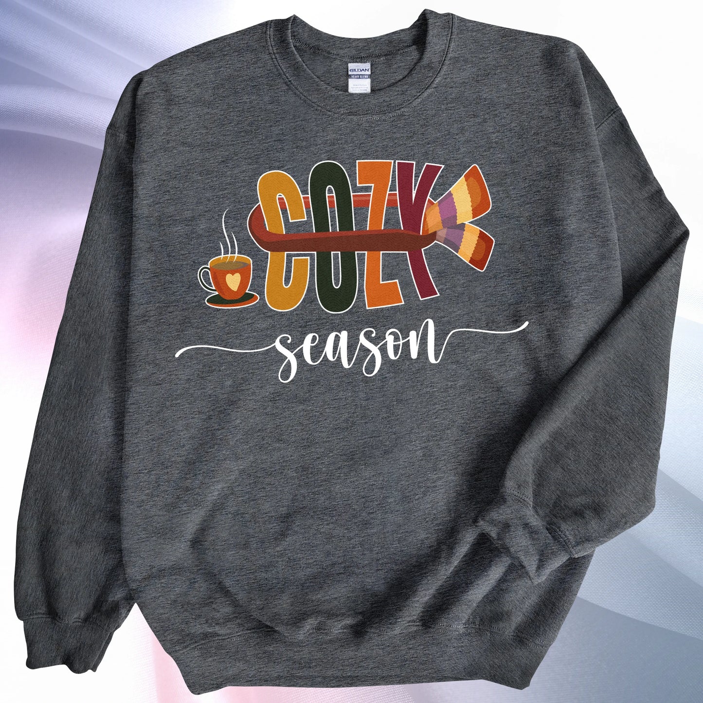 Dark heather Cozy Season sweatshirt, on colorful gradient silk background. Left sleeve folded over the garment at the elbow