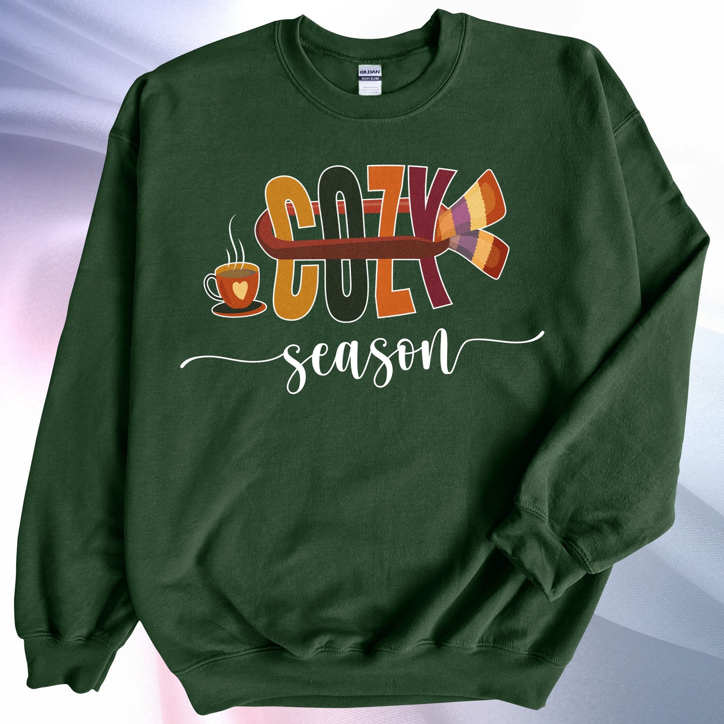 Forest green Cozy Season sweatshirt, on colorful gradient silk background. Left sleeve folded over the garment at the elbow