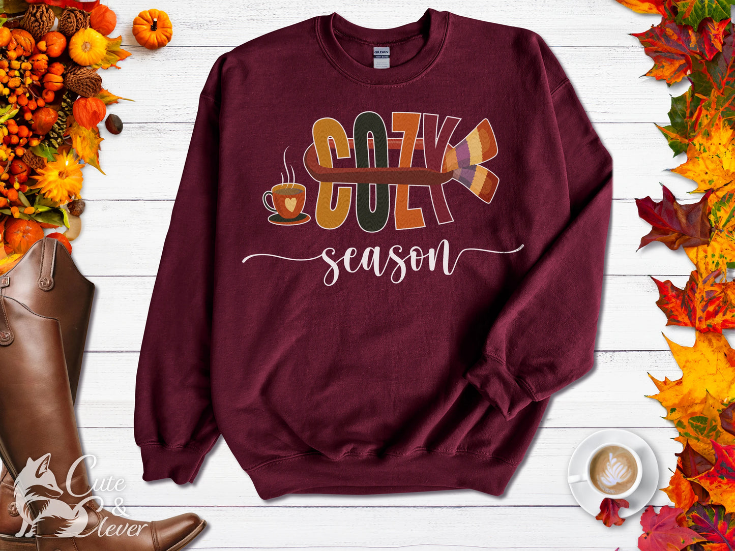 Maroon colored Cozy Season sweatshirt, on colorful gradient silk background. Left sleeve folded over the garment at the elbow