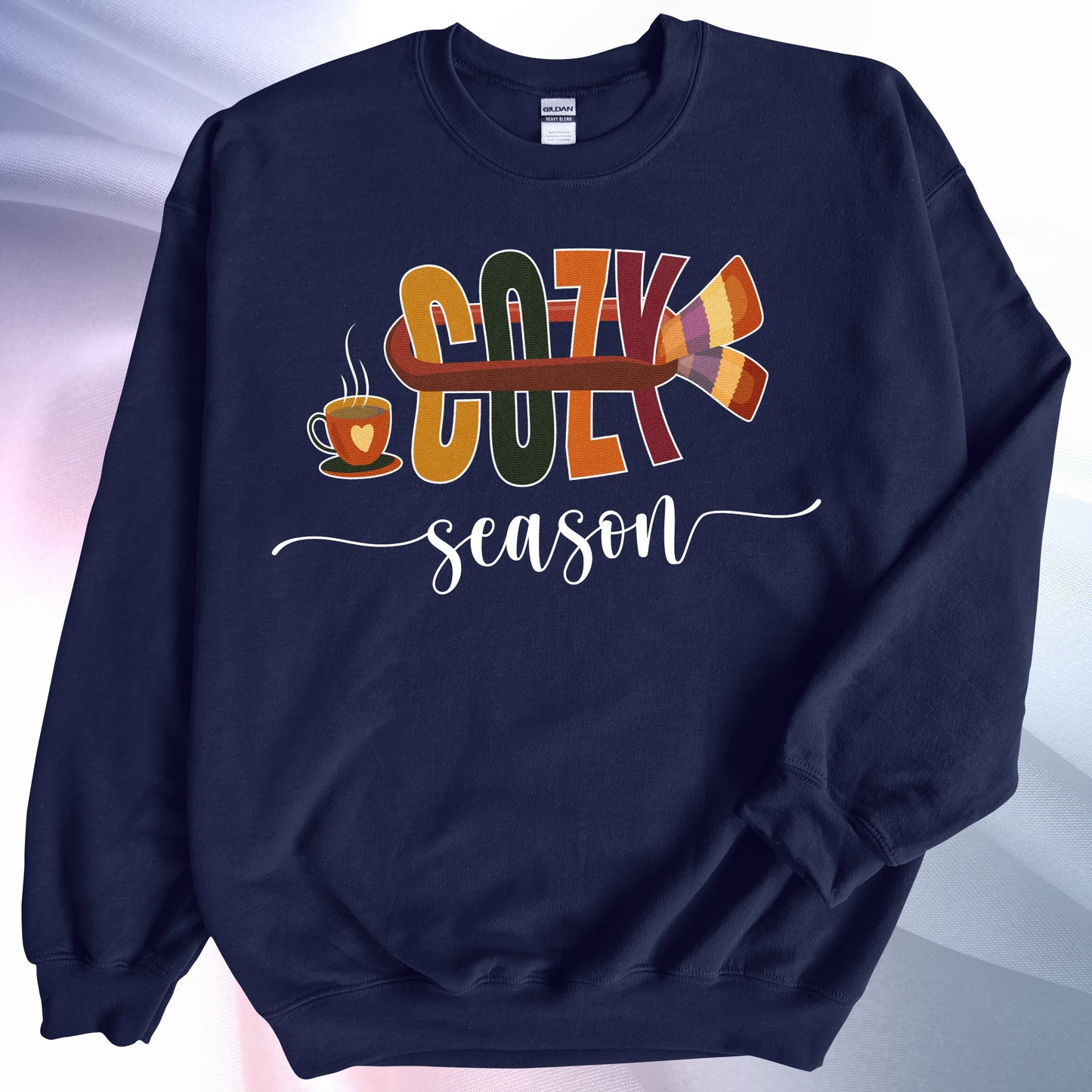 Navy colored Cozy Season sweatshirt, on colorful gradient silk background. Left sleeve folded over the garment at the elbow