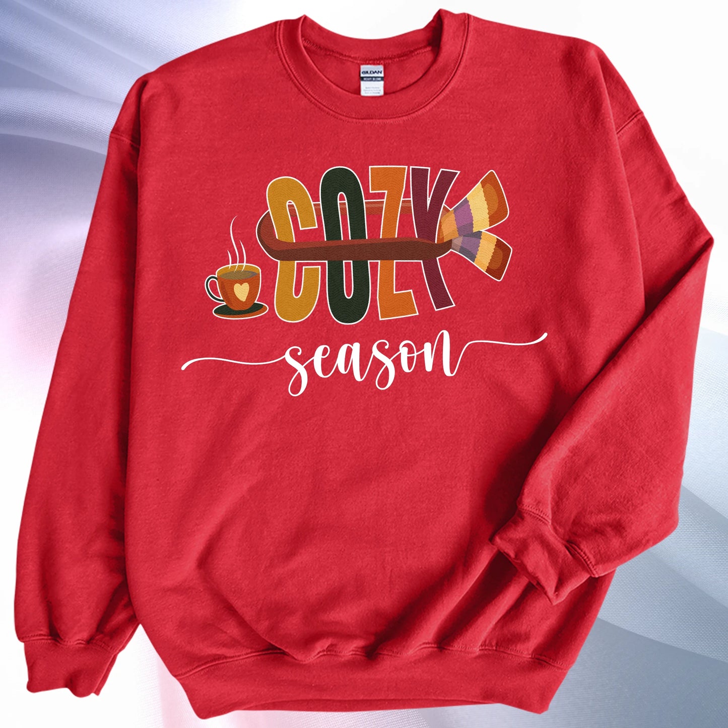 Red Cozy Season sweatshirt, placed on colorful gradient silk background. Left sleeve is folded over the garment at the elbow