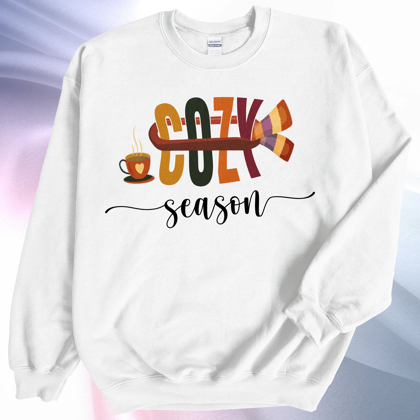 White Cozy Season sweatshirt laying on colorful gradient silk background. Left sleeve is folded over the garment at the elbow