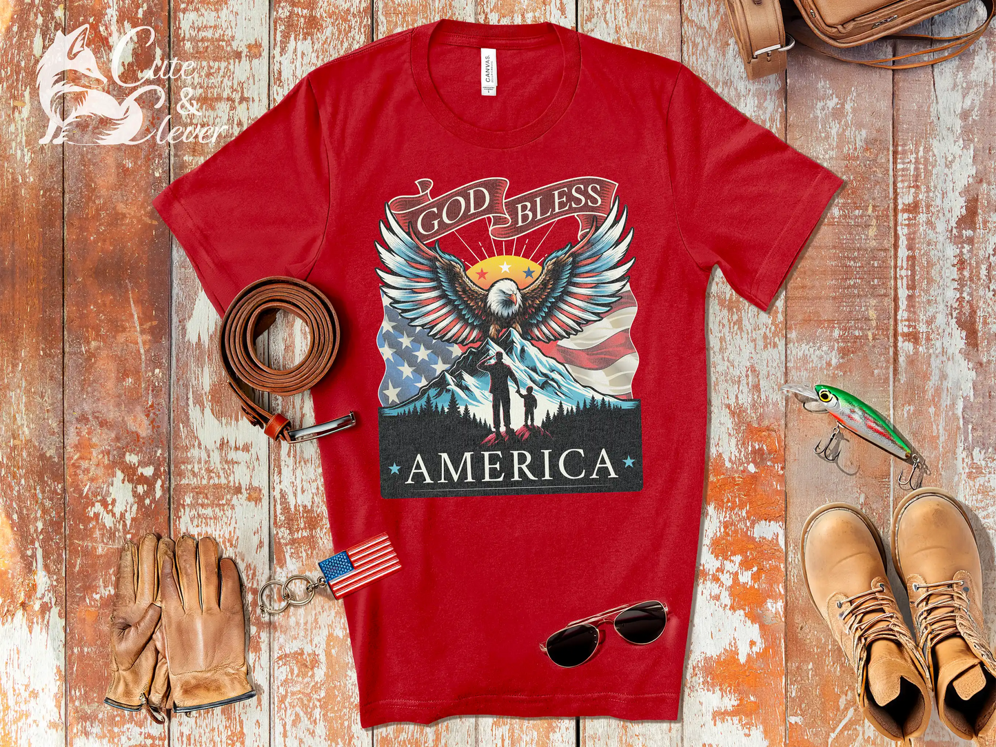 Red Patriotic T-Shirt for Men on rustic wood planks with fishing decor, gloves, rugged boots, sunglasses, belt and flag keychain