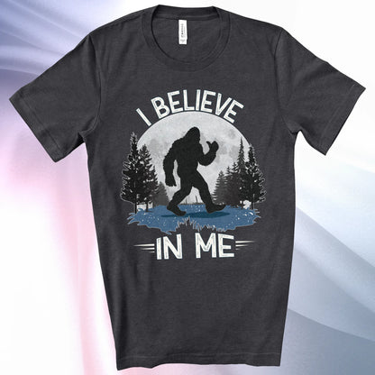 Dark Grey Heather Bigfoot Believes T-Shirt with Bigfoot's silhouette in a moonlit forest and I Believe at the top and In Me below