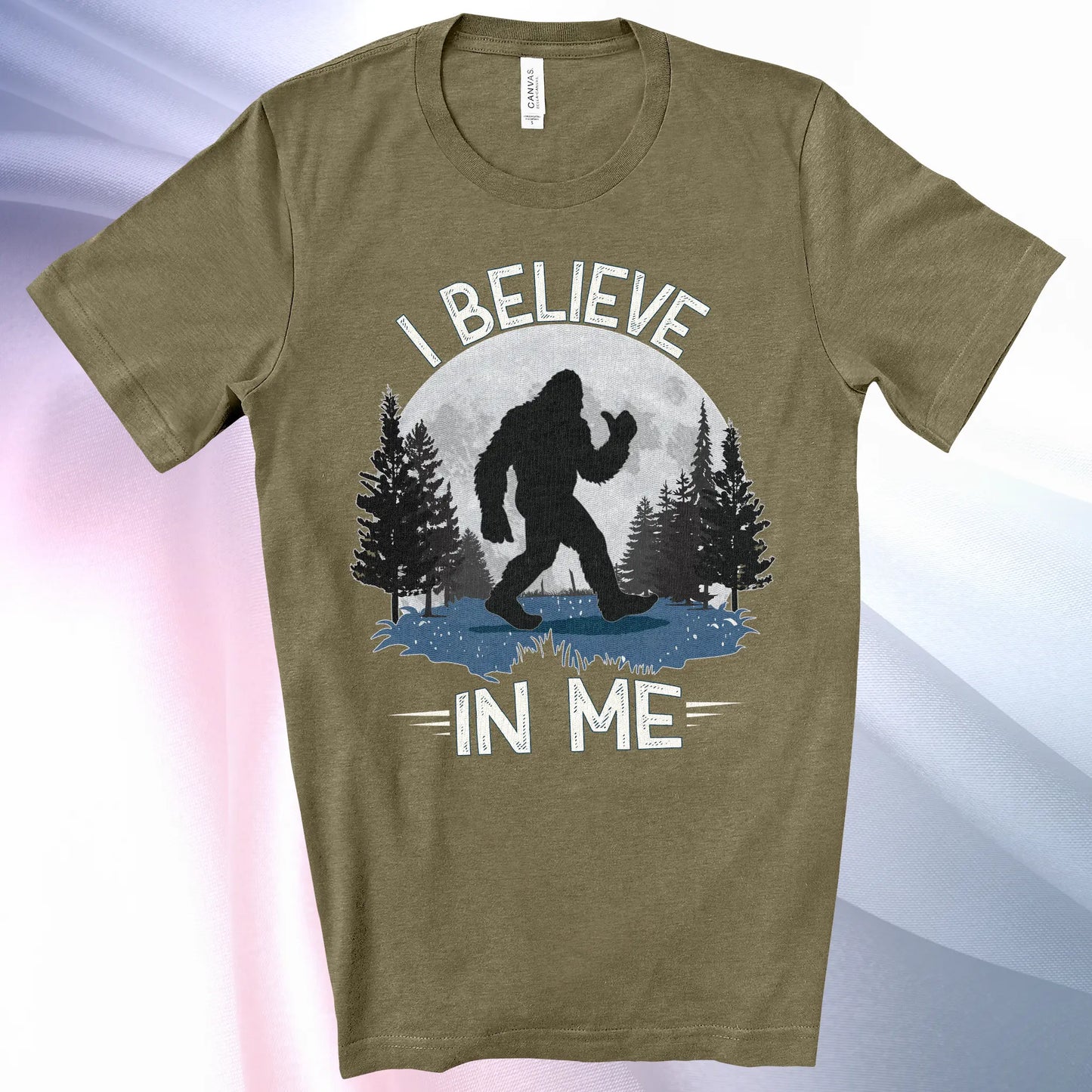 Heather Olive Bigfoot Believes T-Shirt with Bigfoot's silhouette in a moonlit forest and I Believe at the top and In Me below