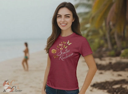 Woman wears Heather Raspberry colored Scatter Kindness T-Shirt while walking outdoors on a tropical beach and enjoying the wind and waves
