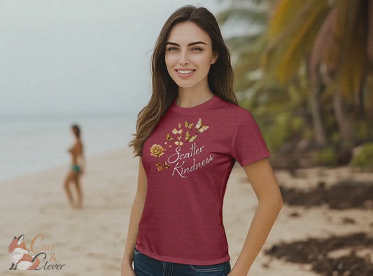 Woman wears Heather Raspberry colored Scatter Kindness T-Shirt while walking outdoors on a tropical beach and enjoying the wind and waves