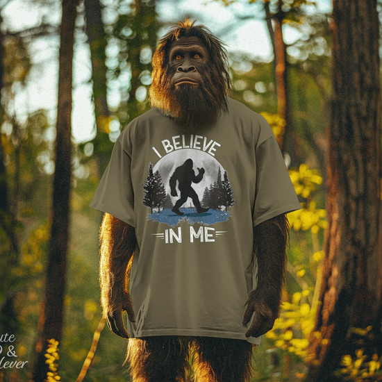 Bigfoot wearing a heather olive Bigfoot Believes T-Shirt in a forest looks slowly from left to right then quickly back toward you!!