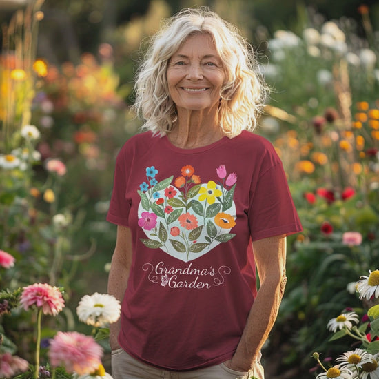 Woman wears Maroon colored Grandma's Garden T-Shirt while walking in beautiful outdoor setting surrounded by flowers